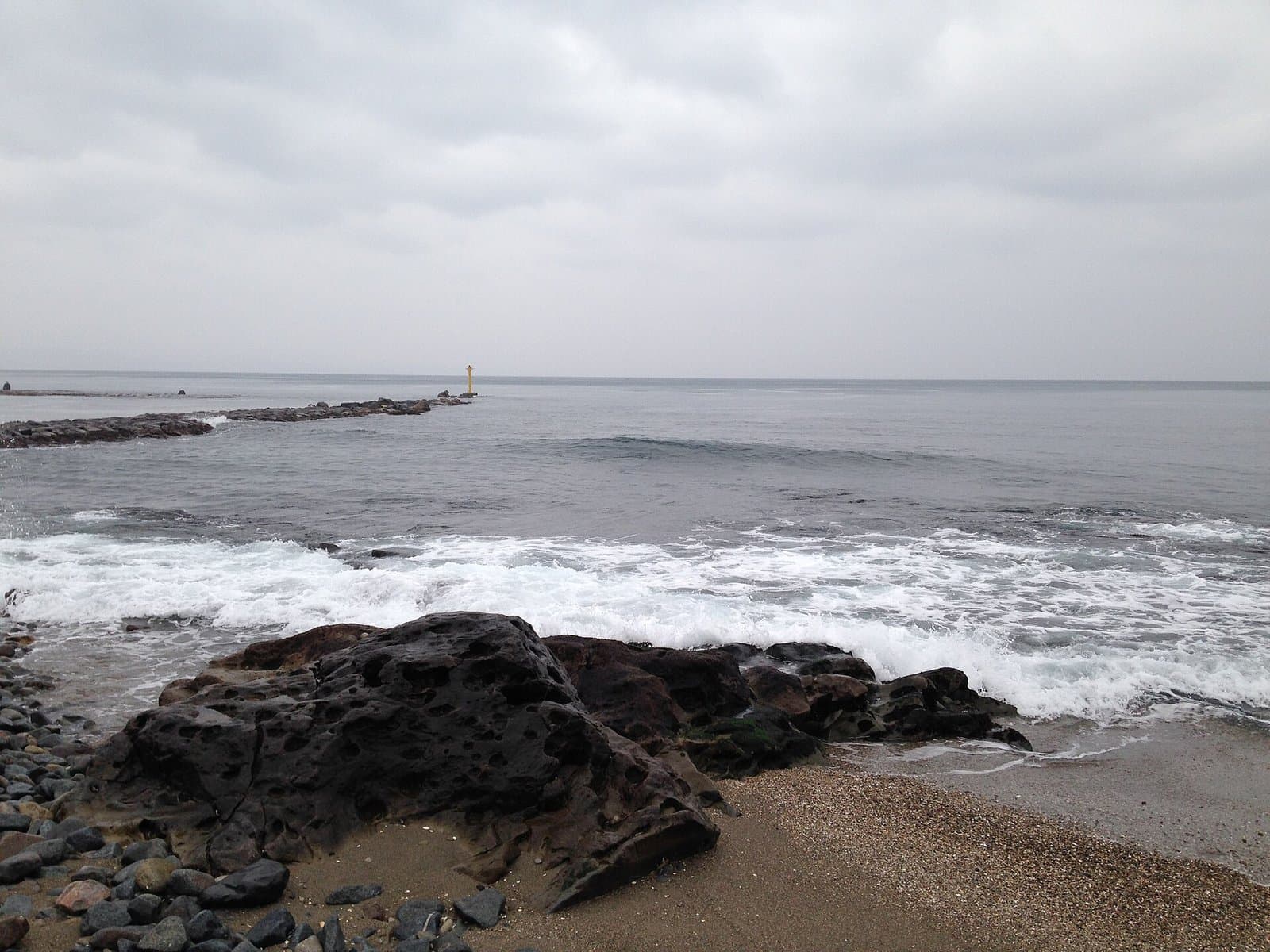 Dark rocks and pebbles on a shore with white waves under a cloudy sky