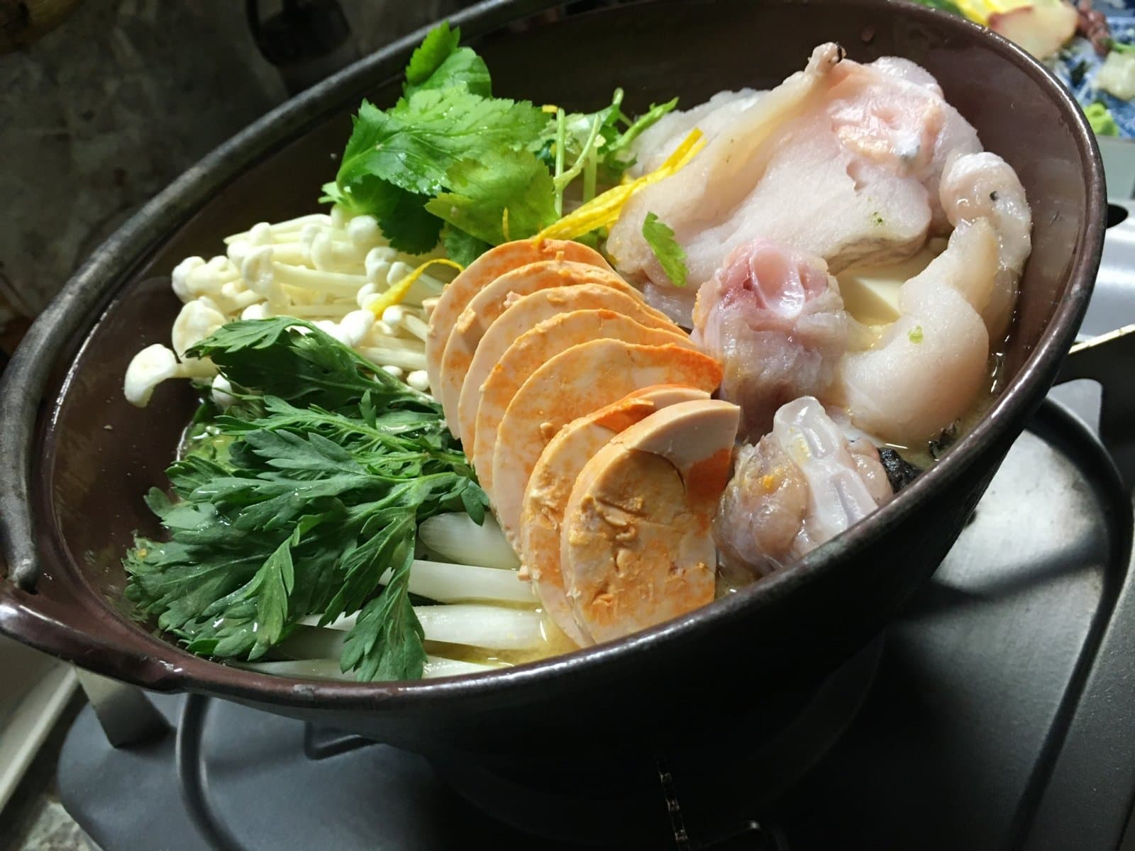 A hot pot with monkfish, sliced monkfish liver, enoki mushrooms, leeks and green leaves