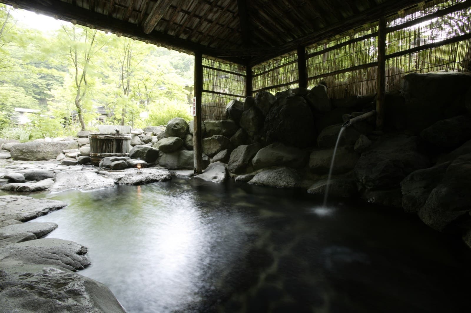 新緑の木々のそばの、屋根付きの岩の露天風呂