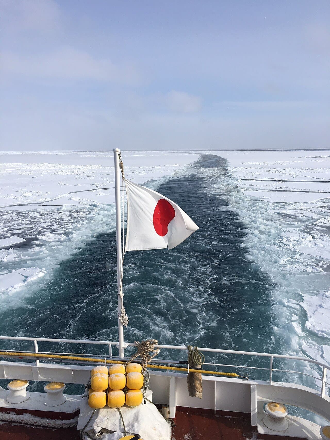 Drift ice on the sea and the ship's wake, seen from the stern with a Japanese flag