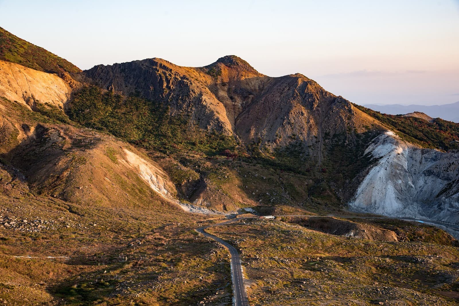 A narrow road winding across bare volcanic slopes lit by the evening sun