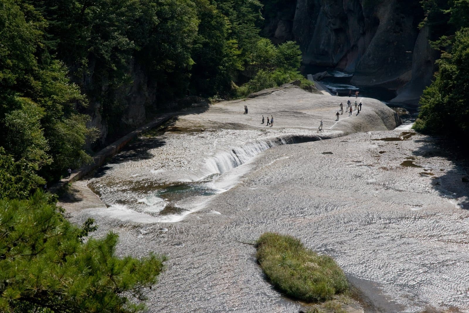 A wide, low waterfall pouring into a crack in a broad flat riverbed of rock, seen from above
