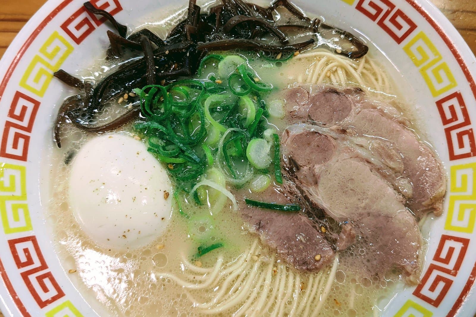 Tonkotsu ramen in a patterned bowl with sliced pork, a boiled egg, green onion and wood ear mushroom