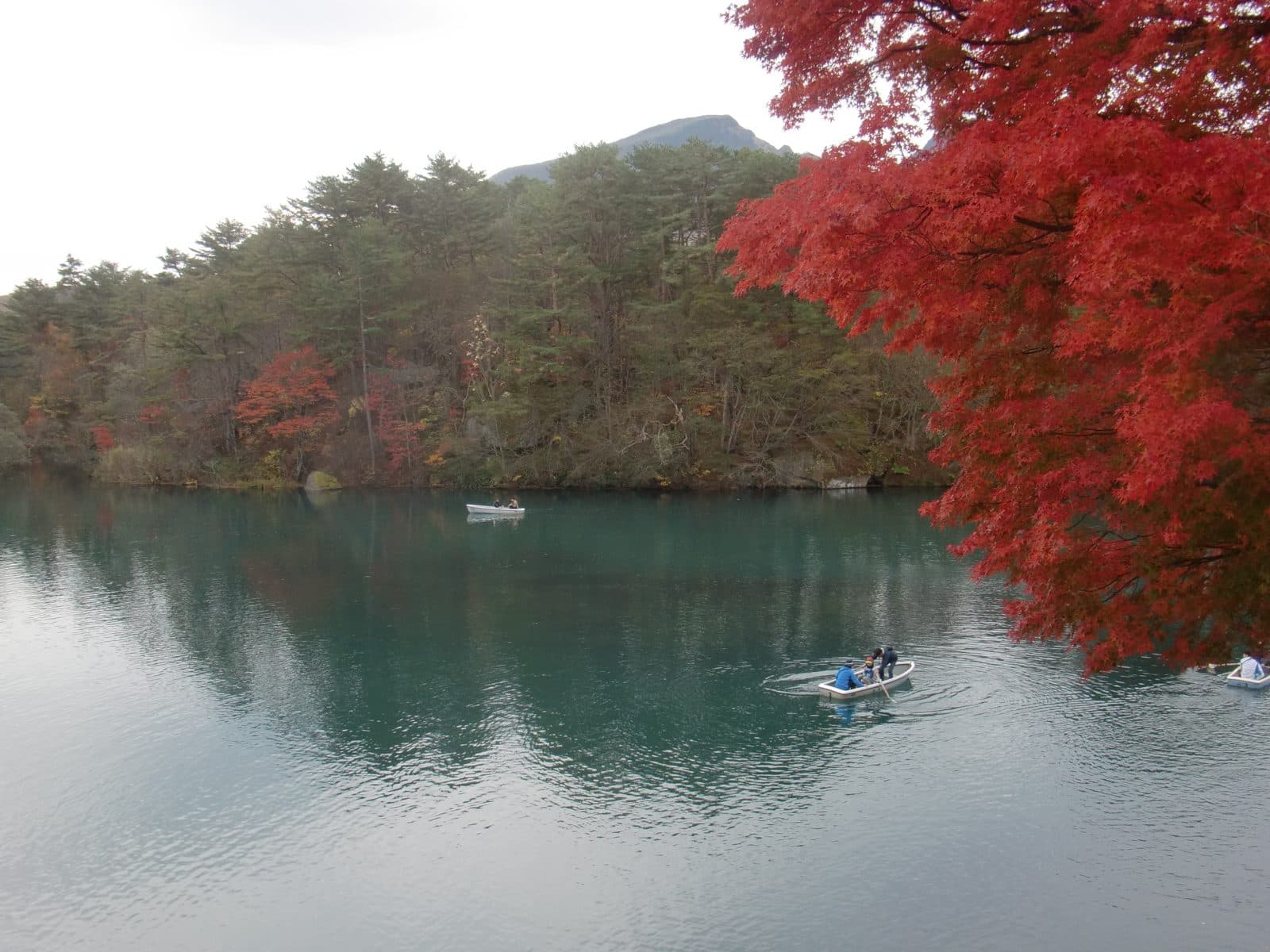 Blue-green Bishamon-numa pond with red maple leaves and small rowing boats