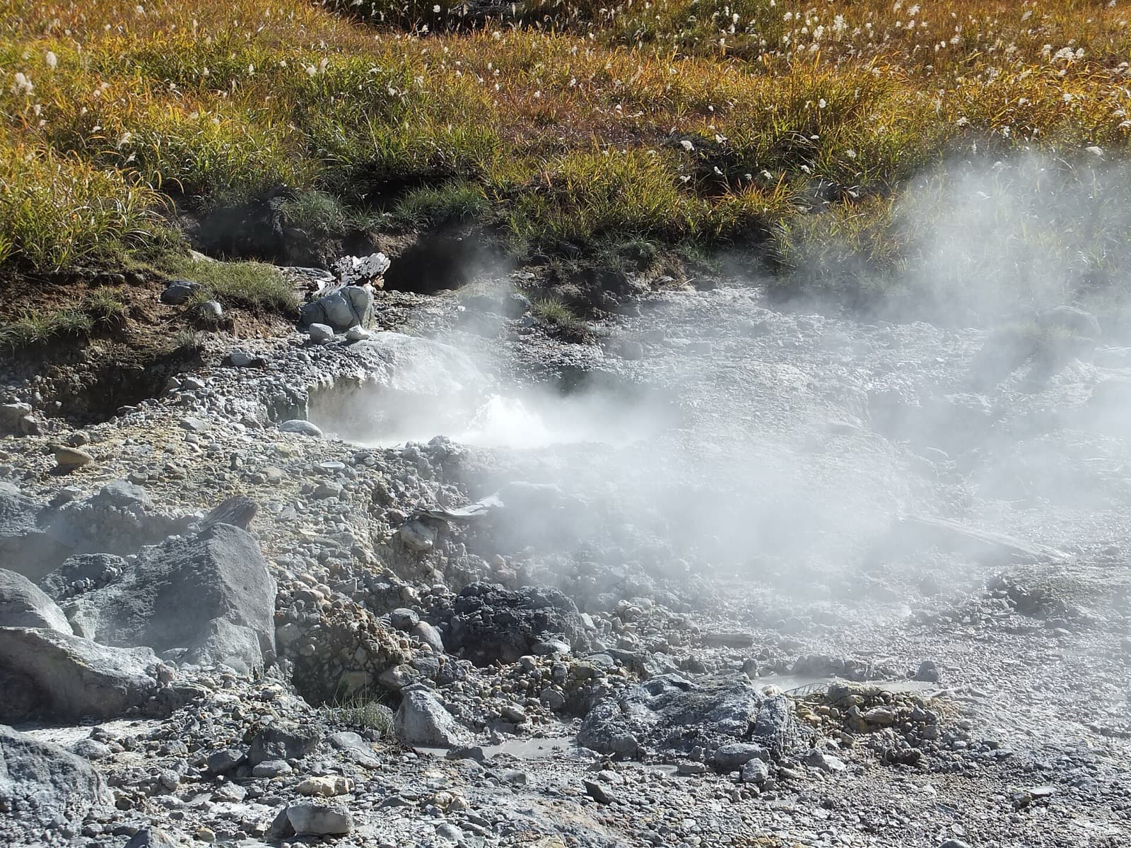 Steam rising from a rocky volcanic valley with dry autumn grass