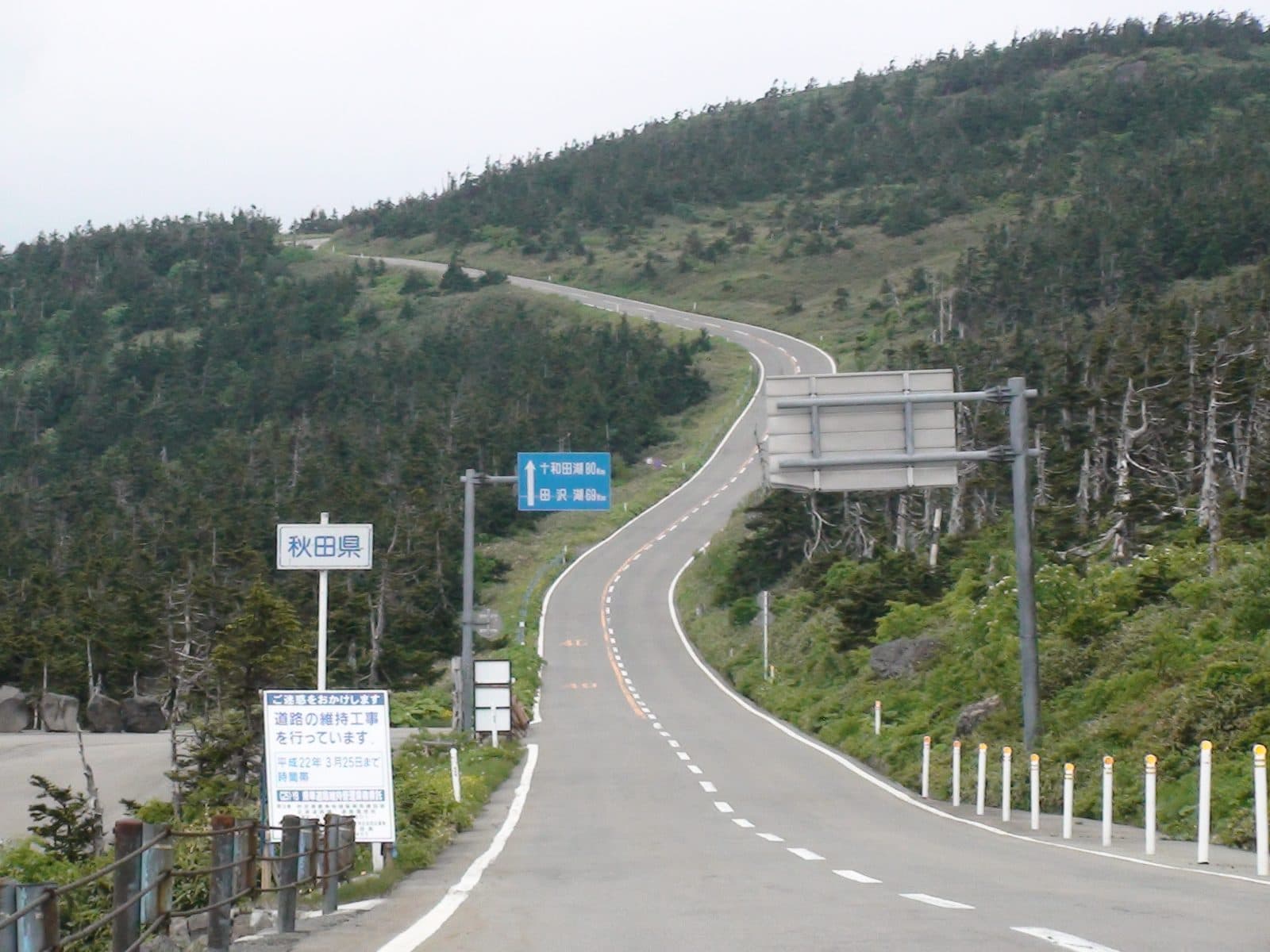 The Aspite Line road curving over a green mountain ridge, with an Akita Prefecture sign