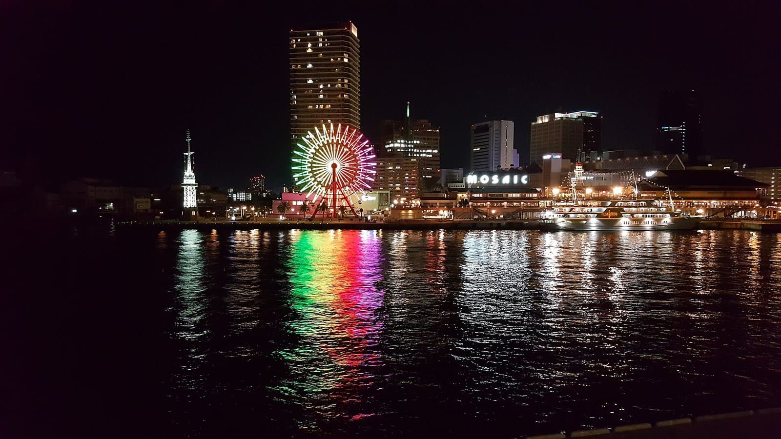 倒映在夜晚海面的彩色摩天輪與海邊建築