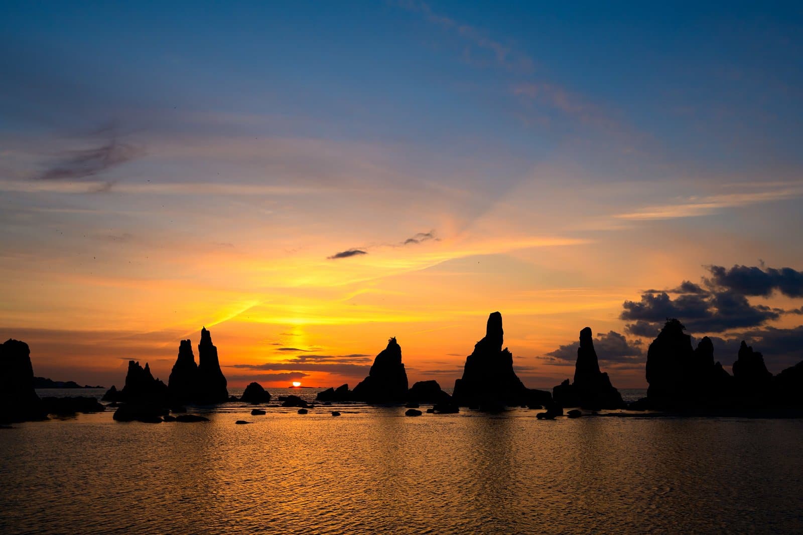 A line of rock pillars silhouetted against an orange sunrise over the sea