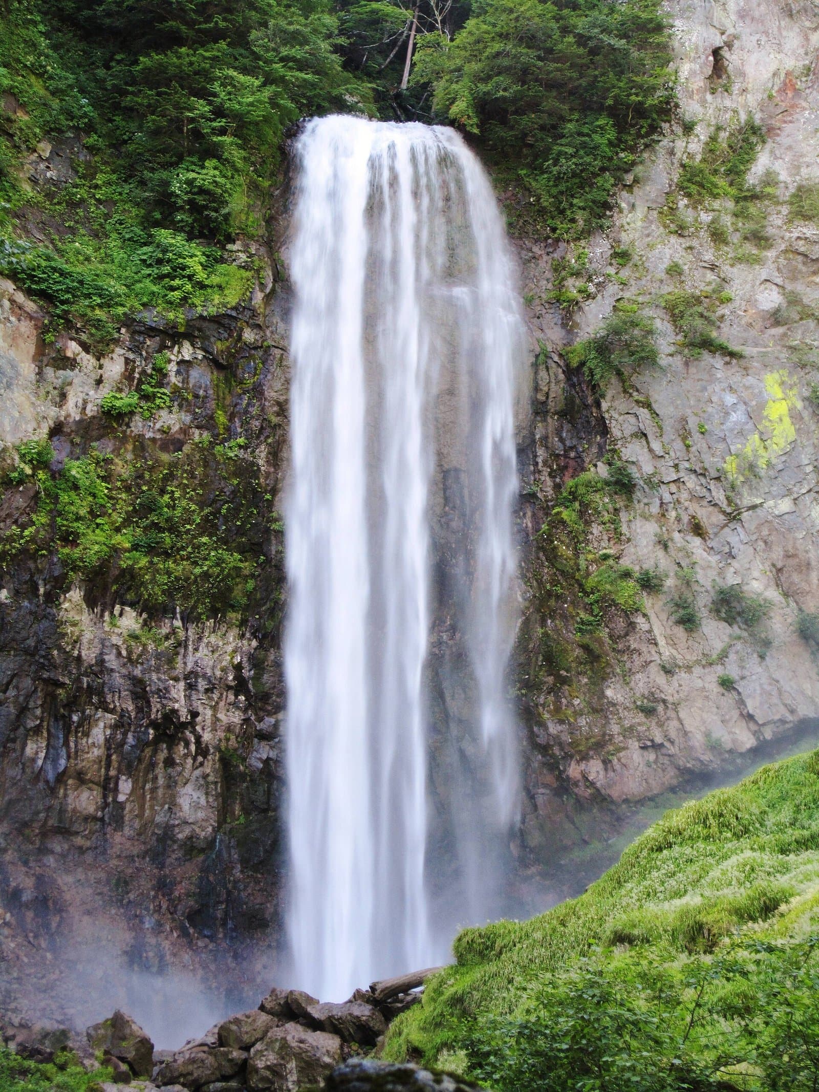 A tall, wide waterfall plunging down a grey rock cliff streaked with green moss
