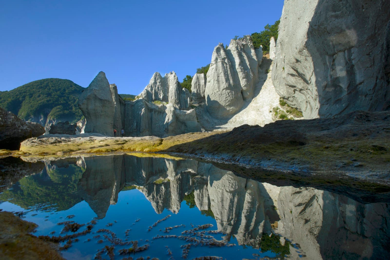 Tall pale rock pinnacles reflected in a still pool under a blue sky