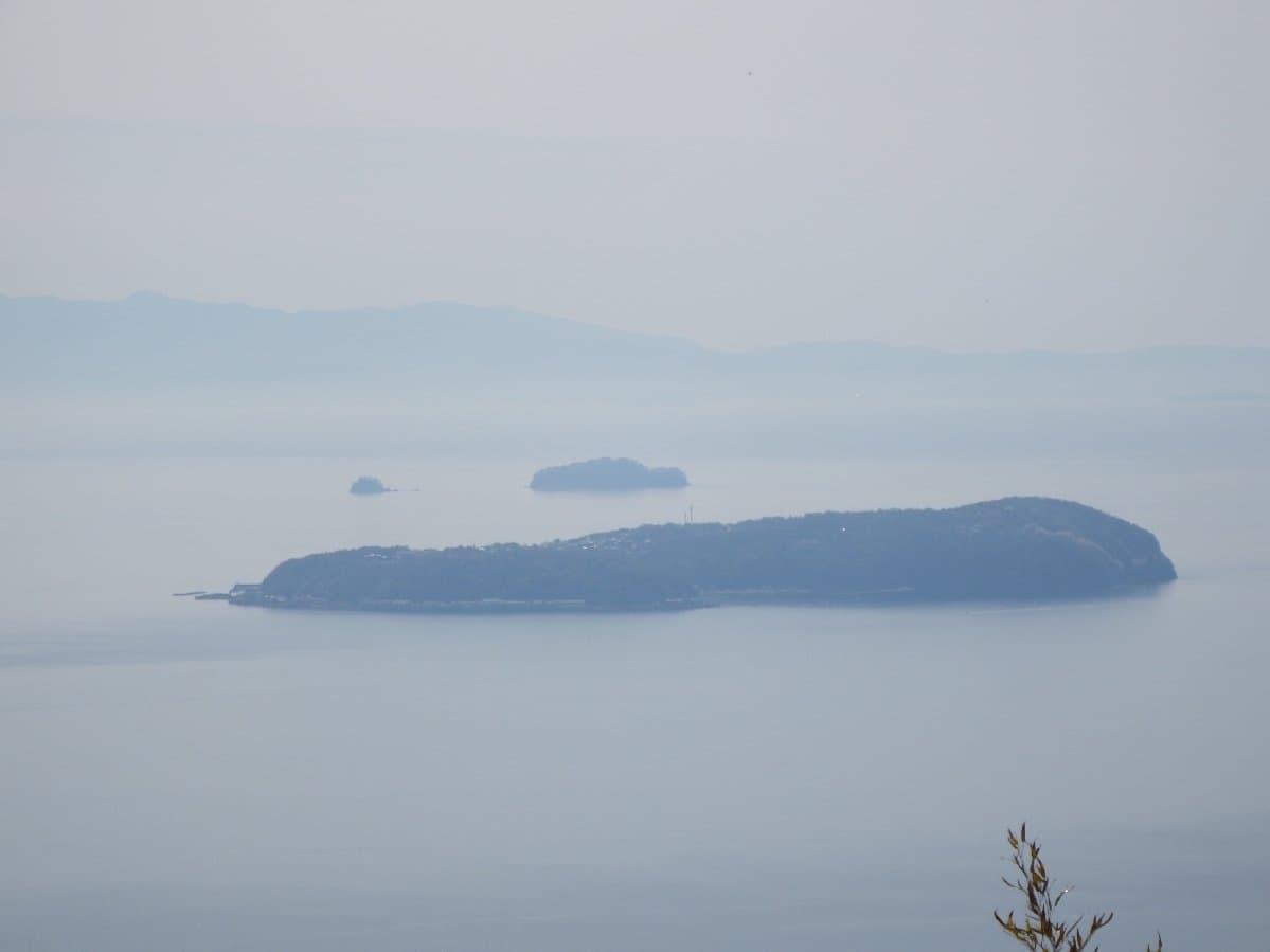 A low island in a hazy calm sea, seen from a mountain