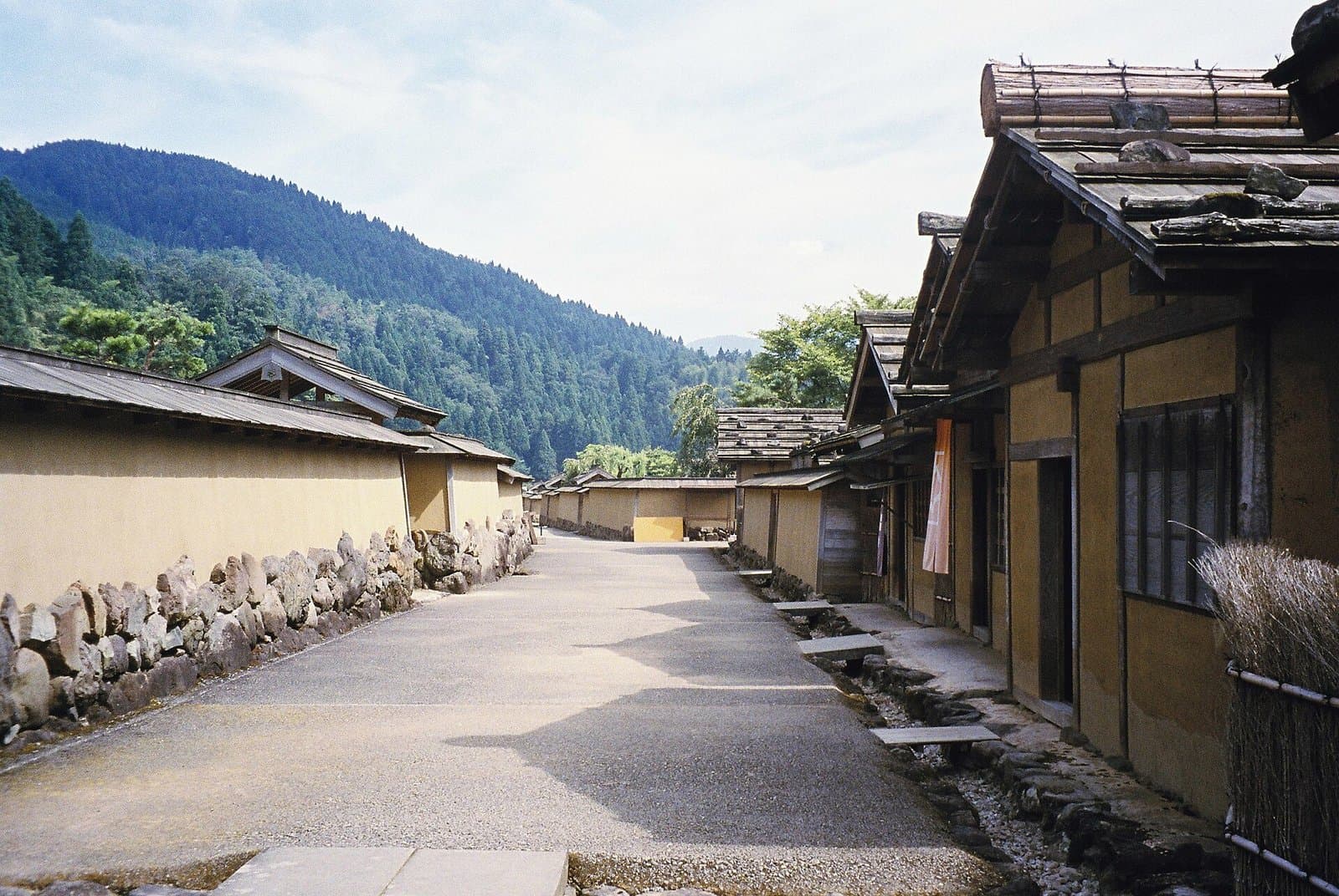 緑の谷の、土塀と古い木造の家が並ぶ砂利の通り
