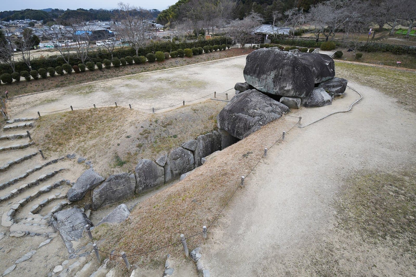 Huge bare stones of the Ishibutai burial chamber and its passage, seen from above, with a village behind