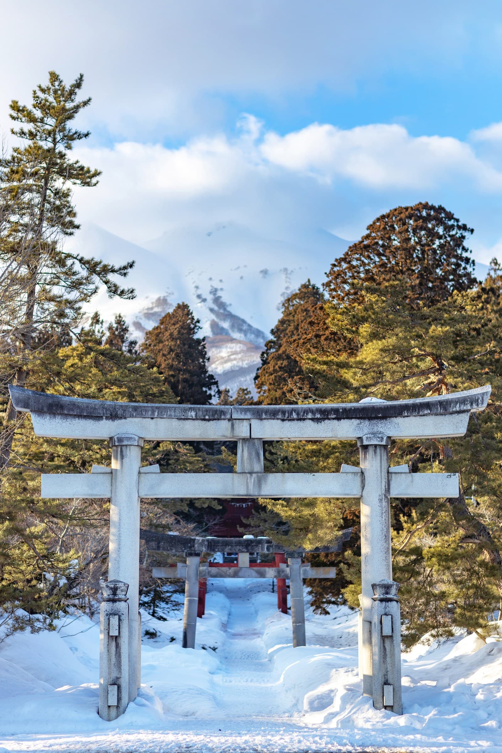 Stone torii gates over a snowy approach, with snowy Mt. Iwaki behind