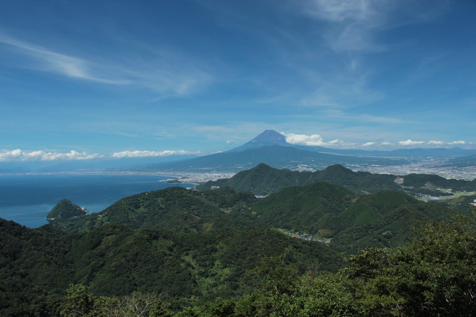 Mt Fuji and Suruga Bay beyond green wooded hills under a blue sky
