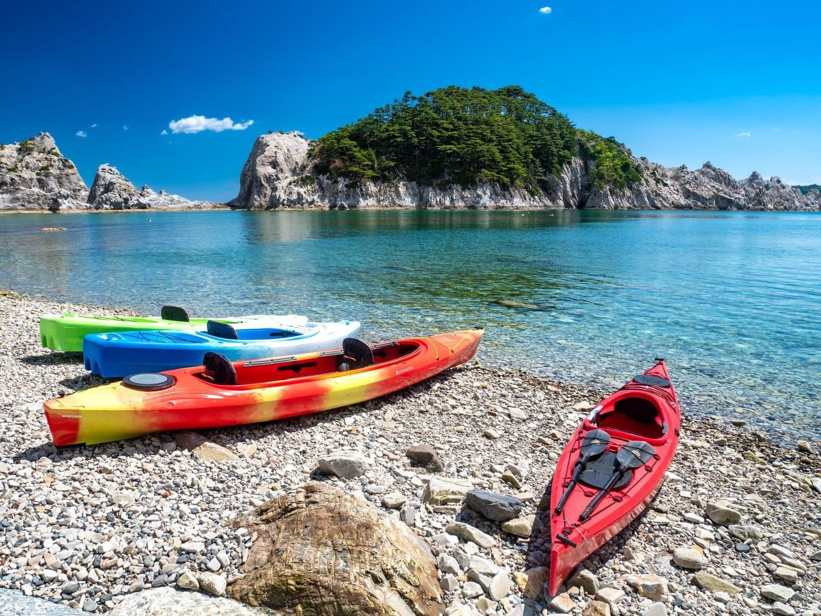 Kayaks on the pebble beach at Jodogahama, with white rock islets and clear blue sea