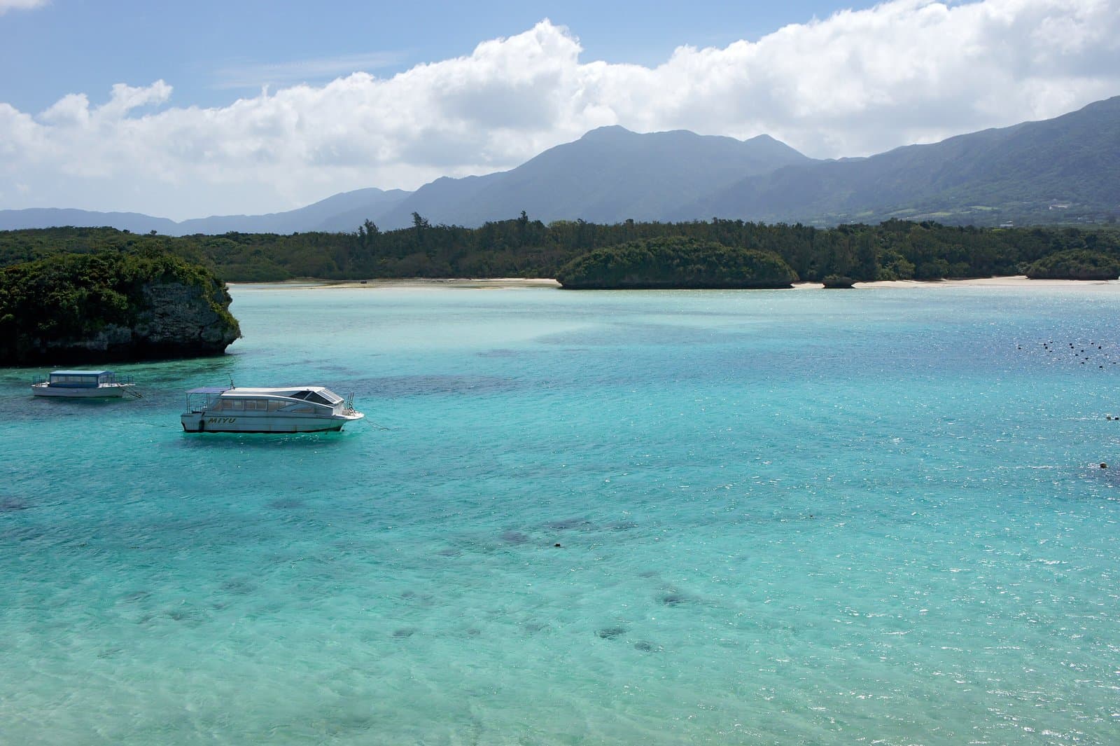 A turquoise bay with small wooded islands, a glass-bottom boat and mountains behind