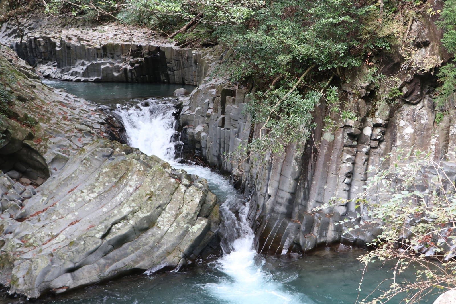 A waterfall rushing between walls of columnar rock into a clear green pool