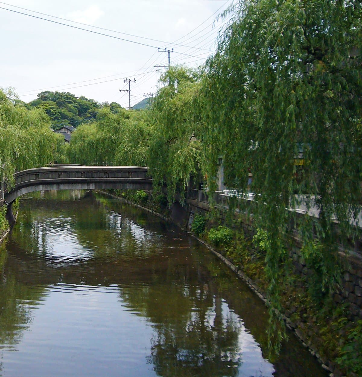 A willow-lined canal with a stone arch bridge