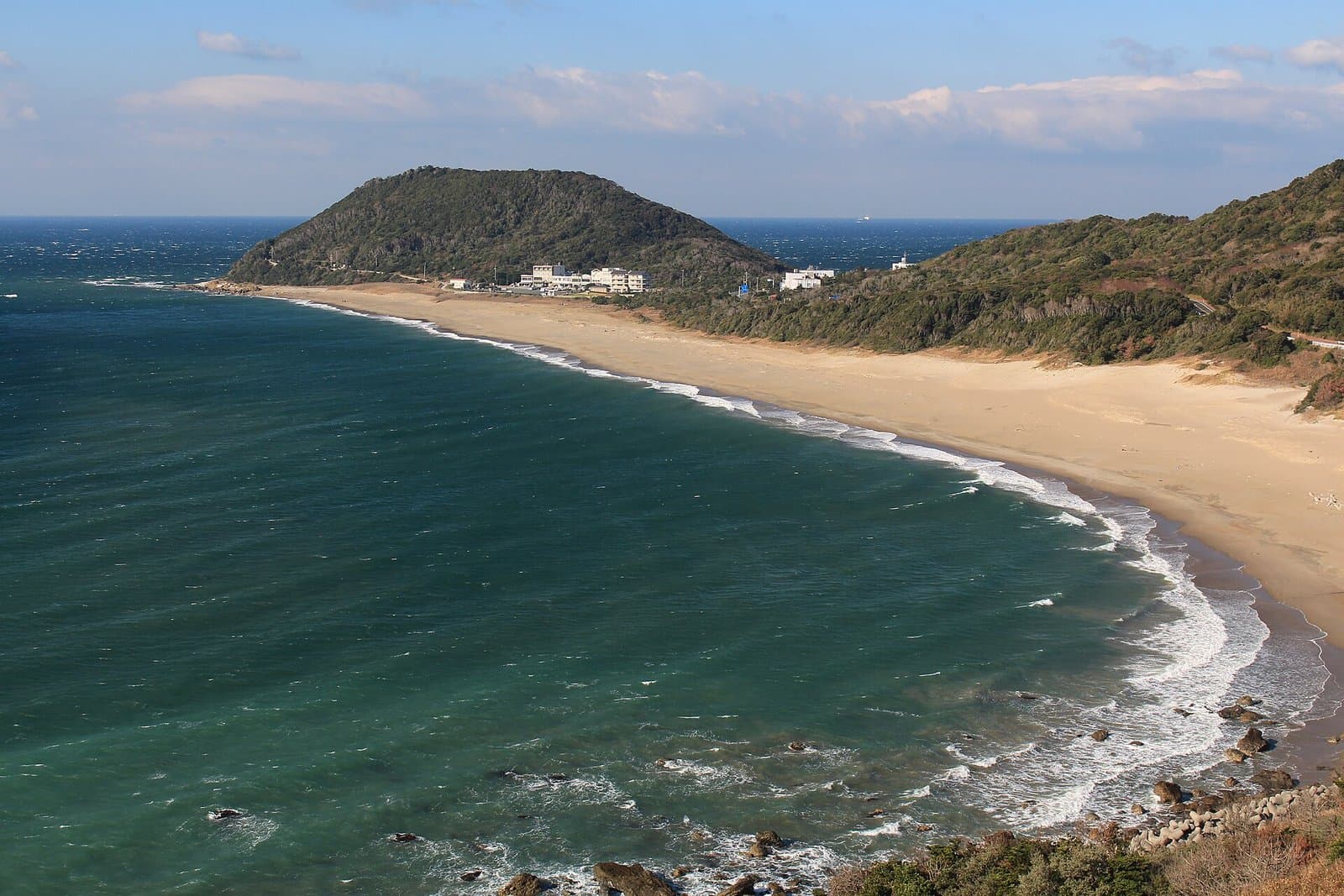 青緑の海に沿って長く弧を描く砂浜と、その先の緑の岬