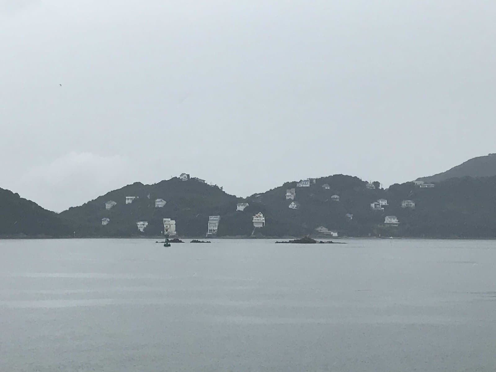A wooded island dotted with white villas across a grey sea on a cloudy day