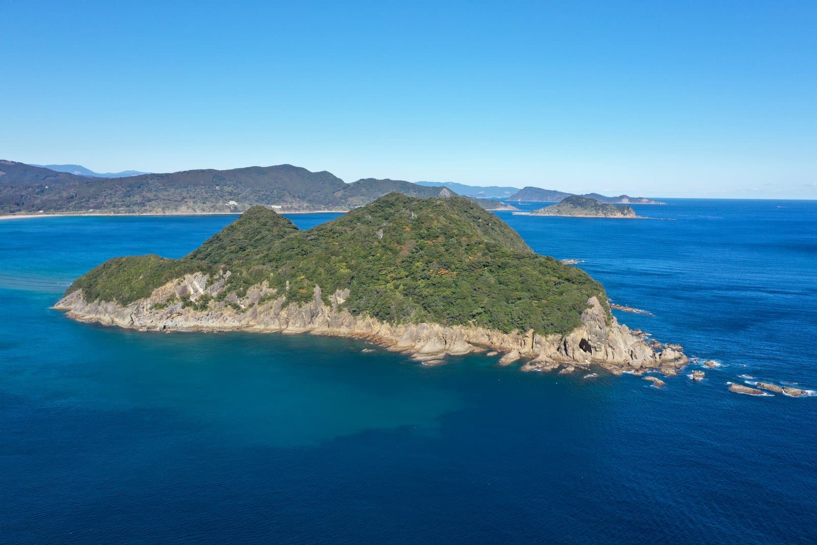A wooded island with rocky shores in a deep blue sea, seen from above