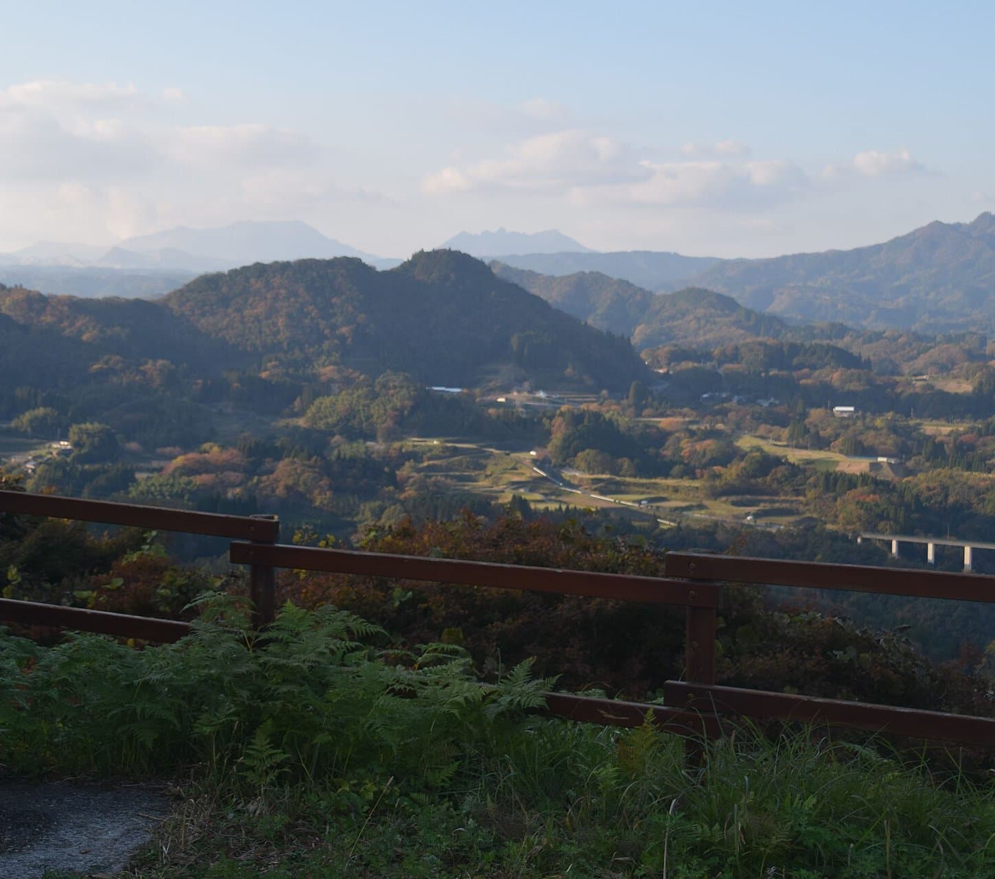 Layers of autumn-coloured hills and farmland with distant mountains, seen over a wooden fence