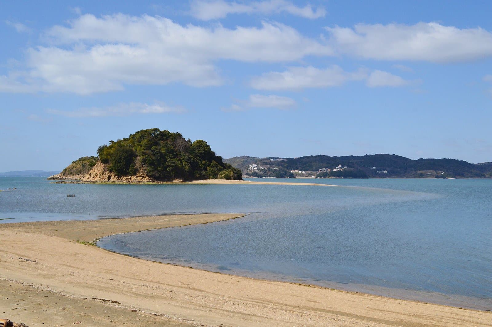 A sandbar path curving across calm water toward a small wooded island