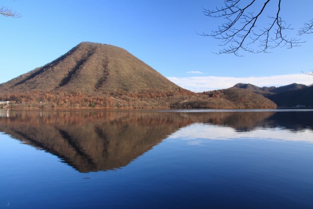 A cone-shaped mountain in late-autumn colours reflected in a calm blue lake