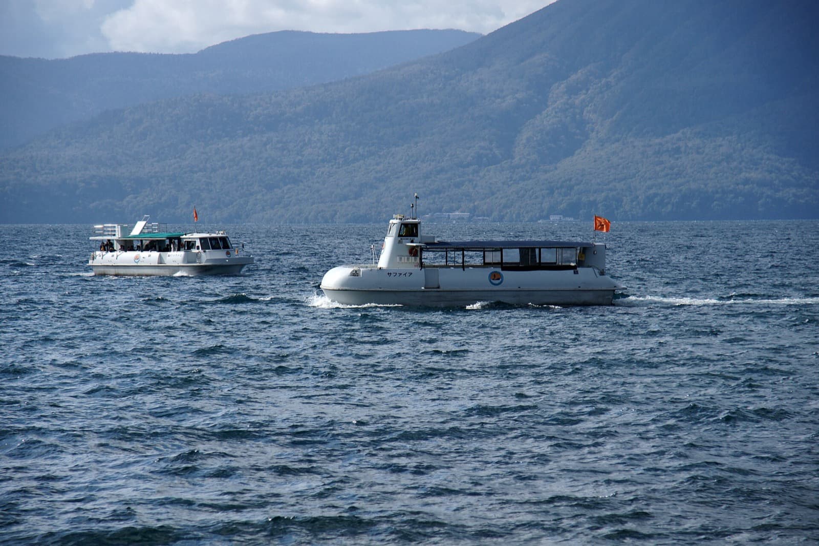 Two white sightseeing boats on the choppy blue lake, with forested mountains behind