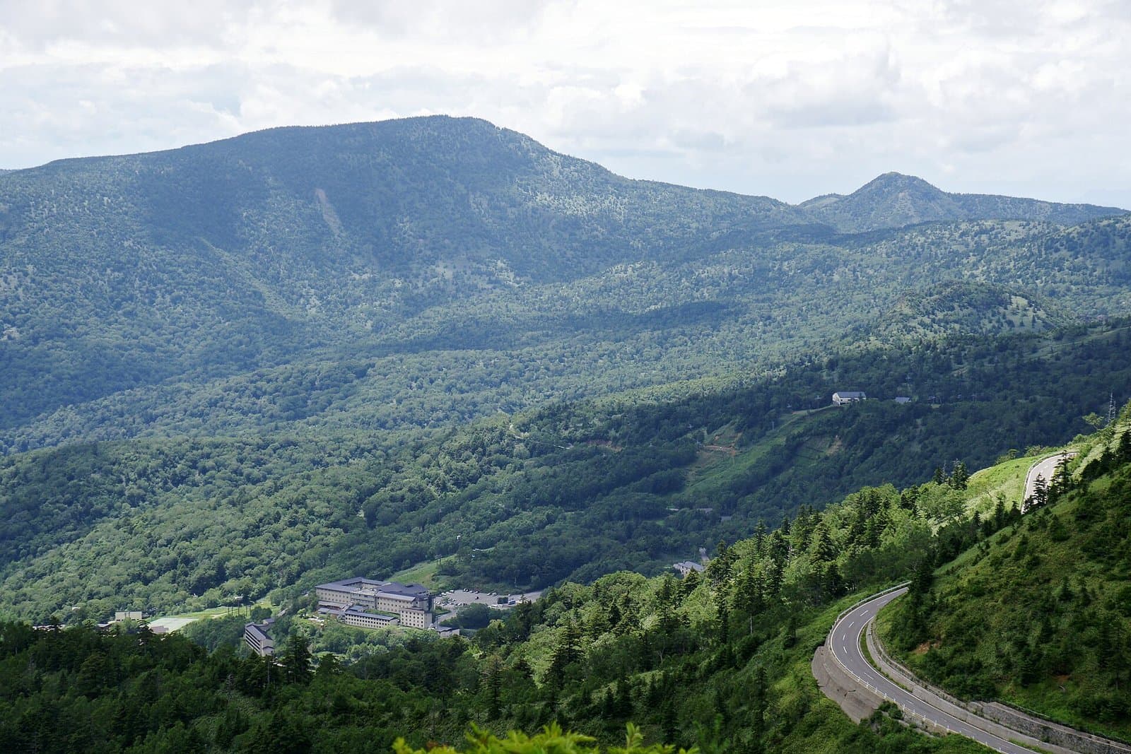 萬座溫泉的建築與上方的森林山巒，右側是蜿蜒的道路