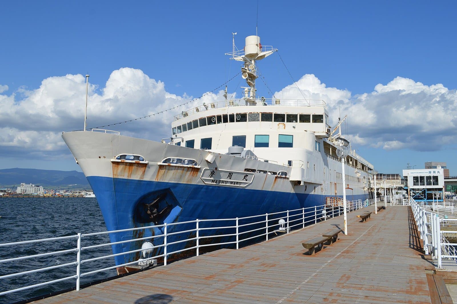 The blue and white ferry Mashu Maru moored beside a wooden pier in Hakodate port