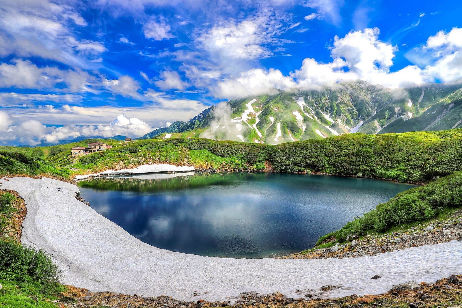 雪の残るふちの深い青の山の池と、奥の岩の峰と雲