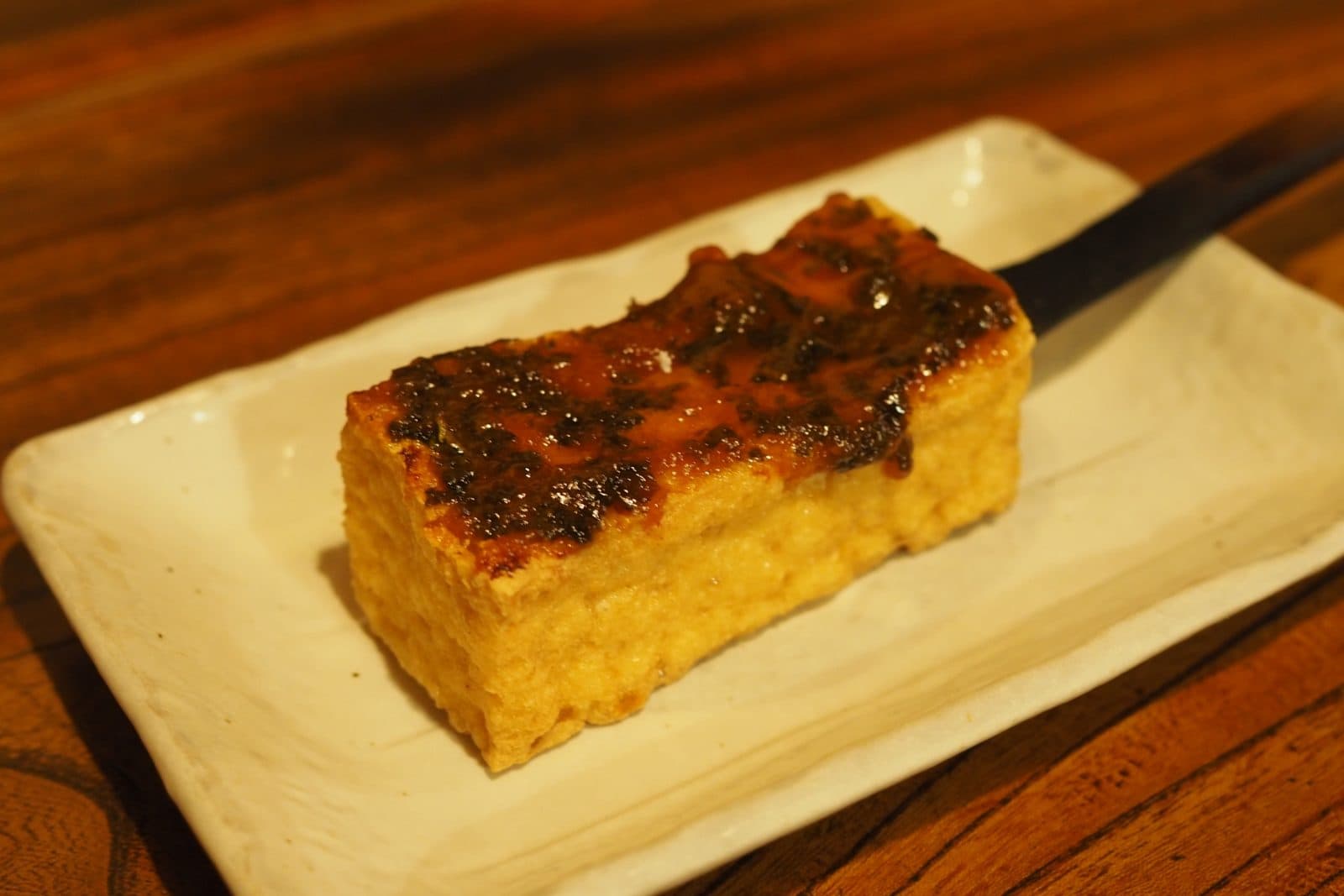 A block of grilled tofu topped with caramelised miso on a white plate