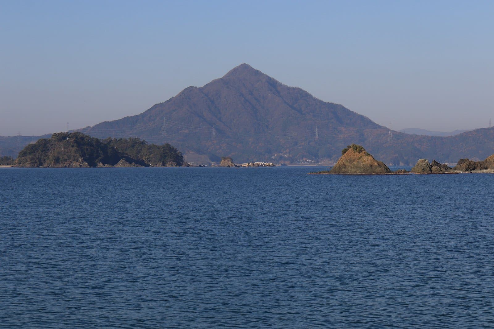 在平靜的藍色海灣與小岩島後方聳立的尖錐形山峰
