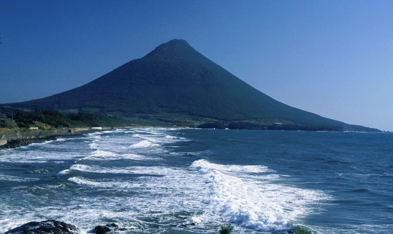 A cone-shaped mountain rising above a coast with white waves