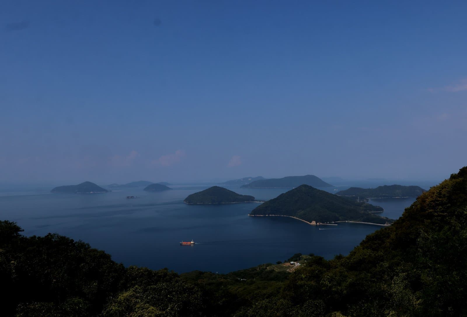 Wooded islands scattered across a calm dark-blue sea, seen from a hilltop