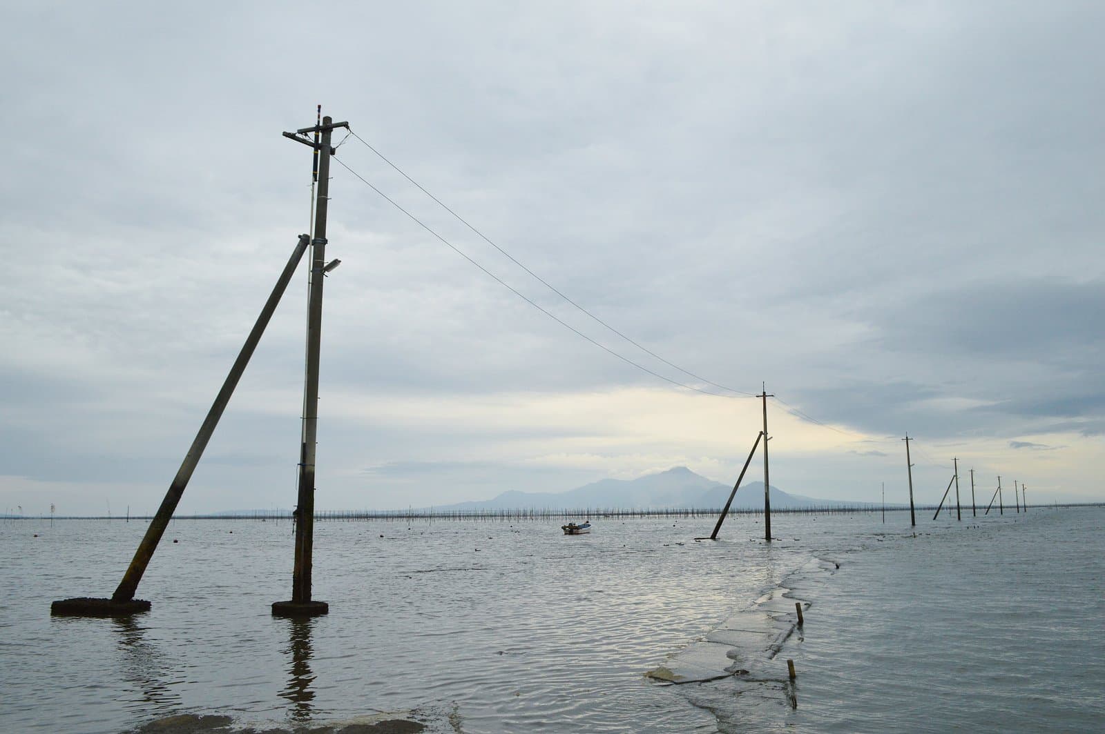 A line of utility poles standing in shallow sea water toward the horizon