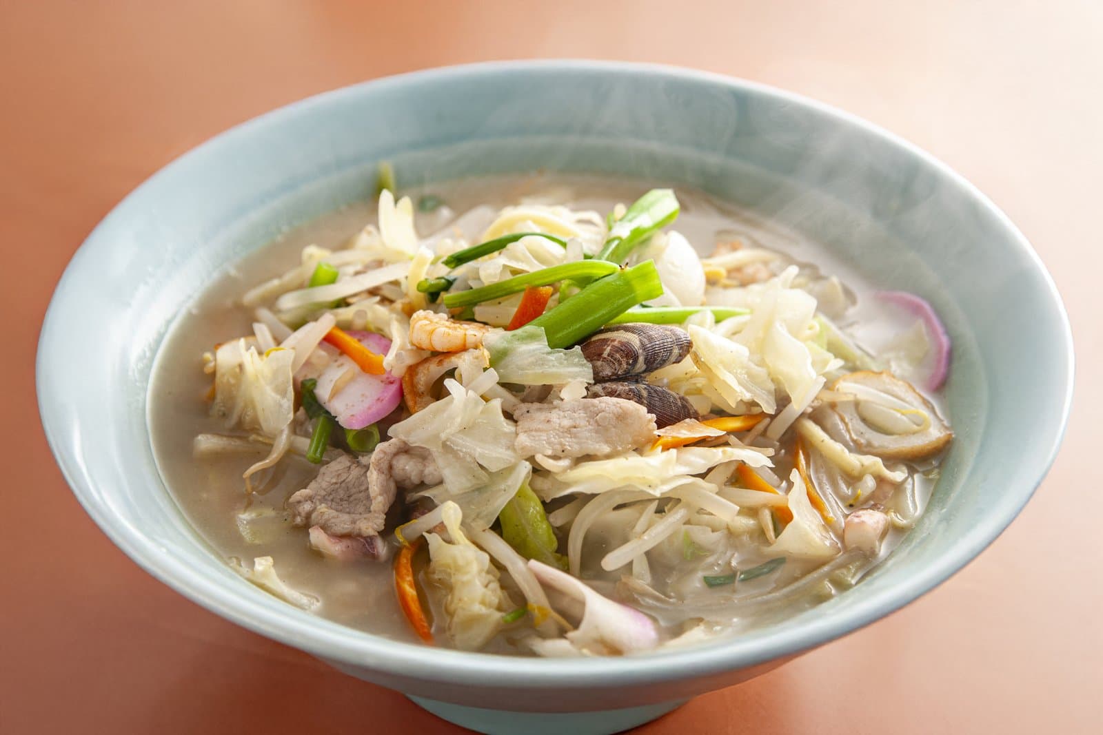 Champon noodles topped with stir-fried cabbage, bean sprouts, pork, seafood and fish cake in a pale bowl