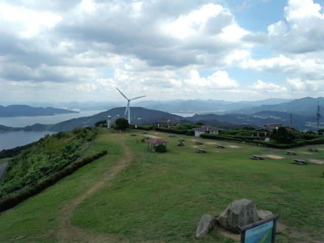 海と山並みを見渡す、テーブルと風車のある草原の丘