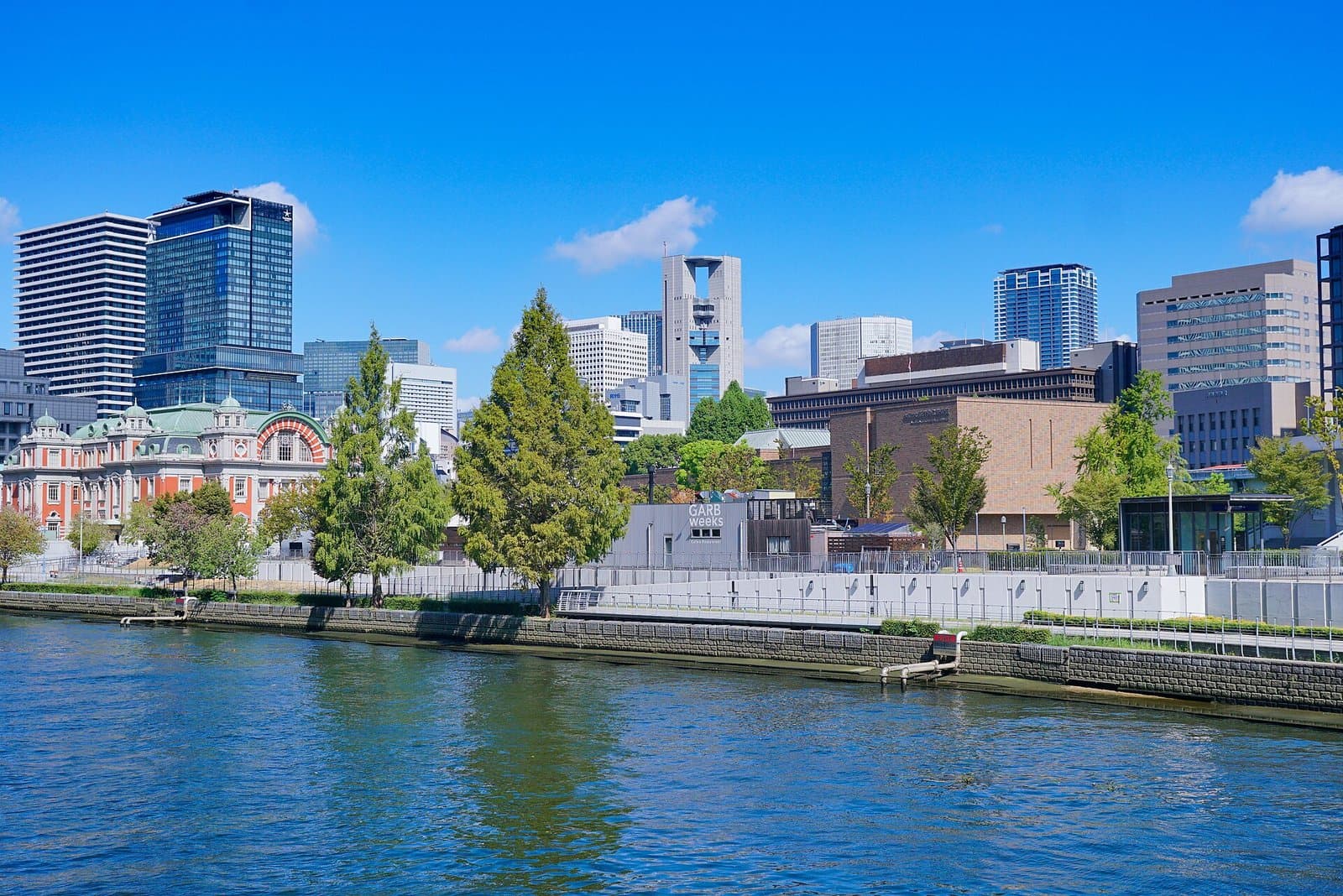A river with a tree-lined bank, the red-brick Central Public Hall on the left and office towers behind
