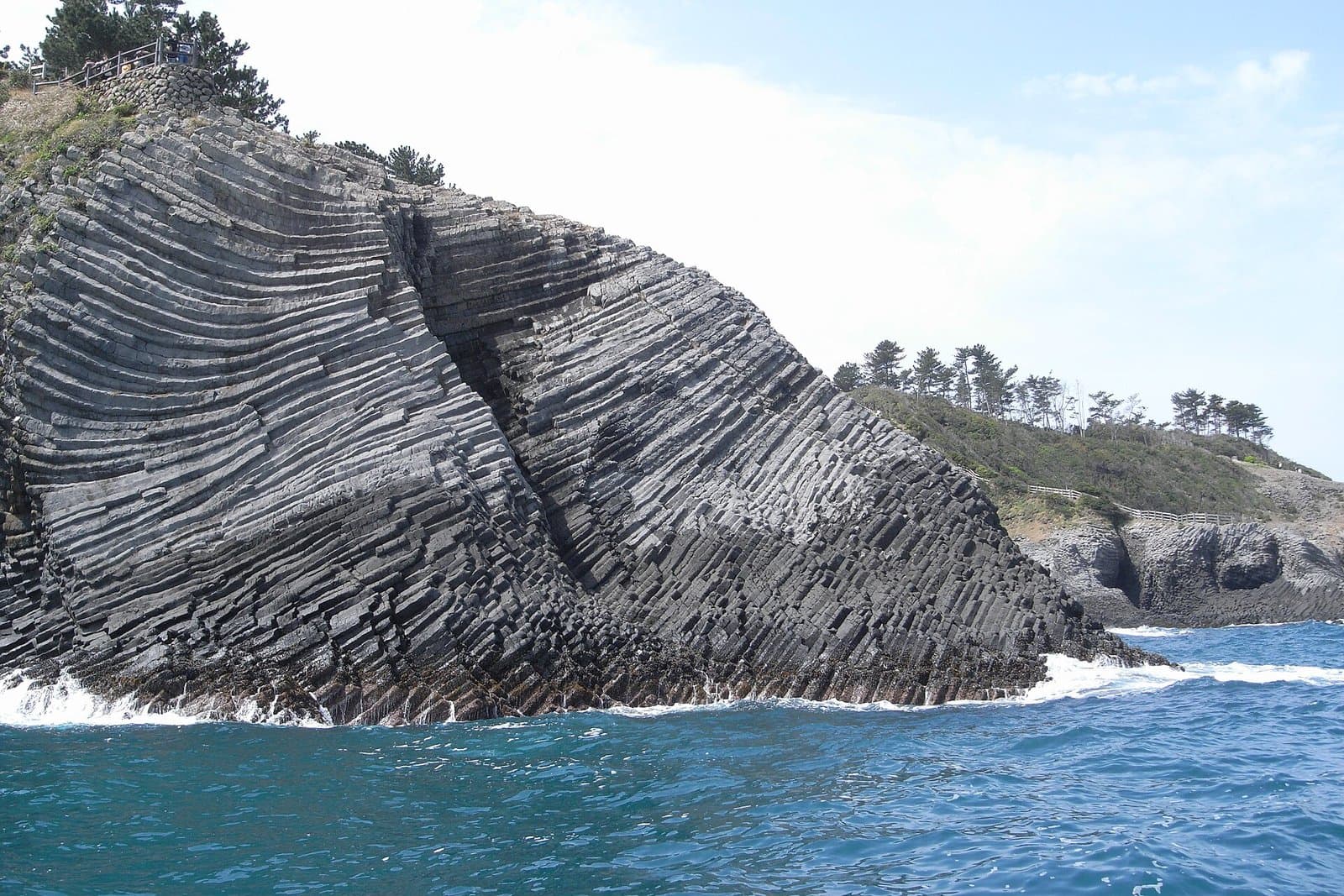 A cliff of columnar basalt rising from a blue sea with white waves