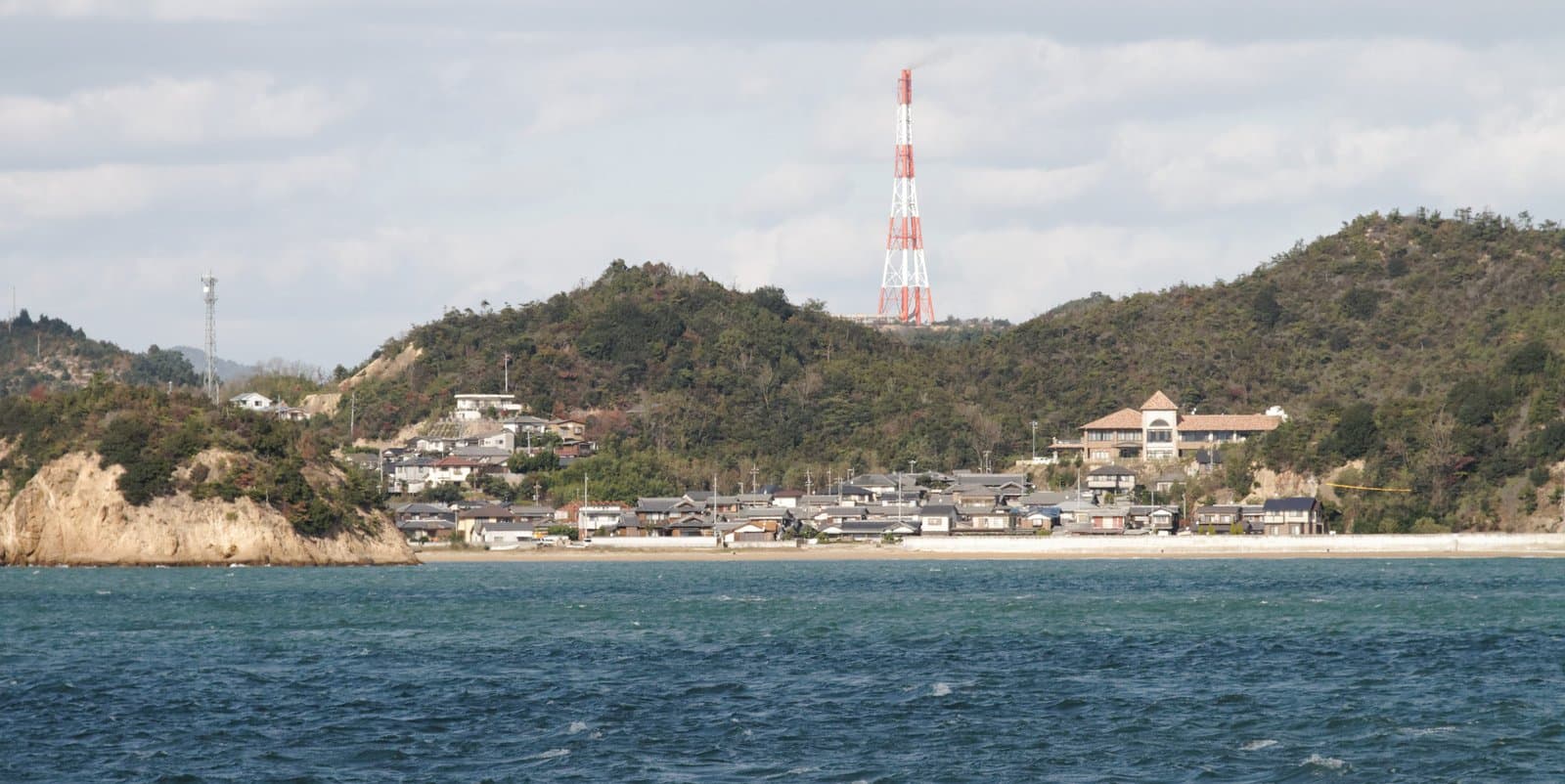 A small seaside village at the foot of green hills, seen across a choppy sea