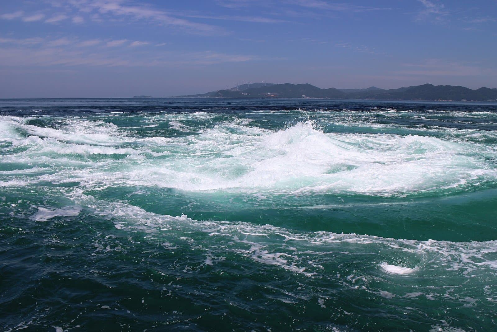 Swirling, foaming green sea currents with hills on the horizon