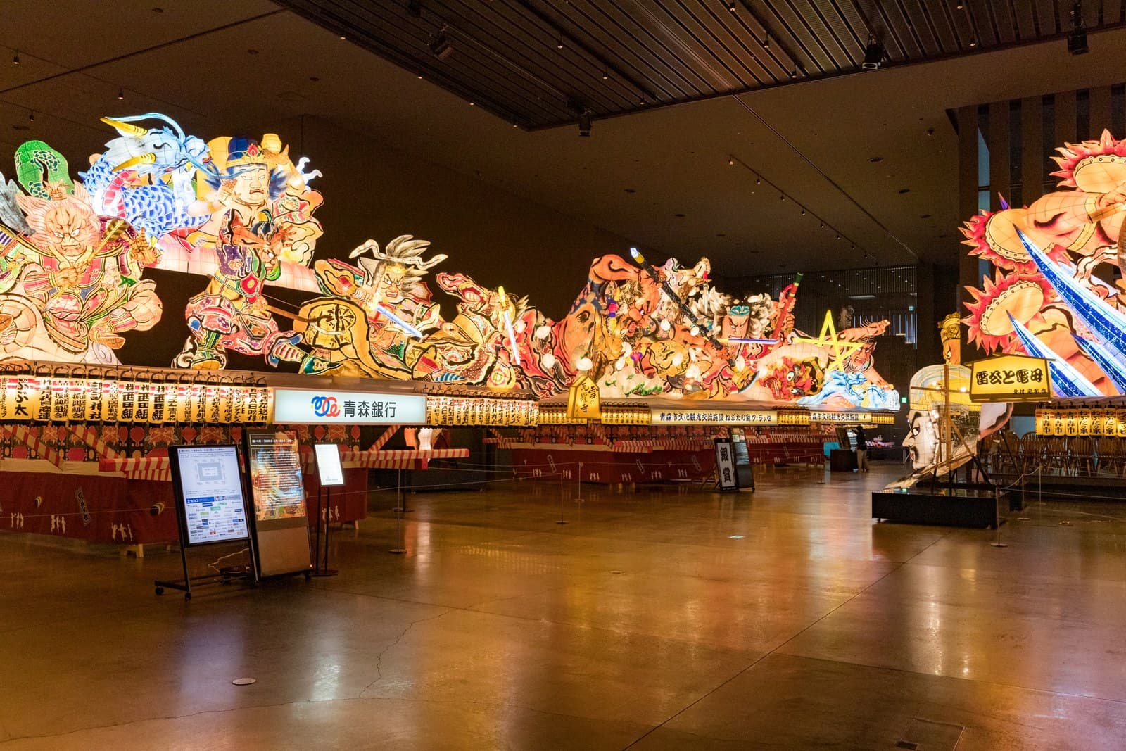 Large lit-up Nebuta floats displayed side by side in a dark hall