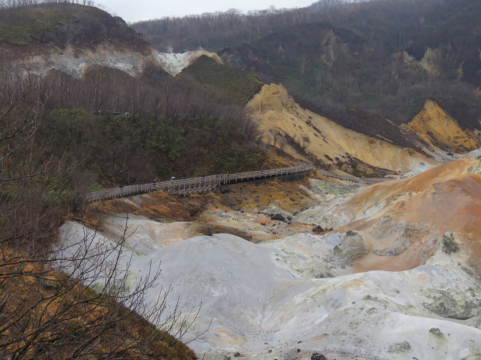 A yellow and white volcanic valley with a wooden boardwalk along the slope