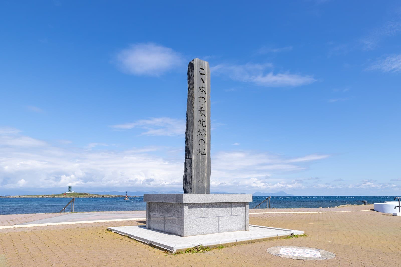 A stone monument marking the northernmost point of Honshu, with the sea and a small lighthouse island behind