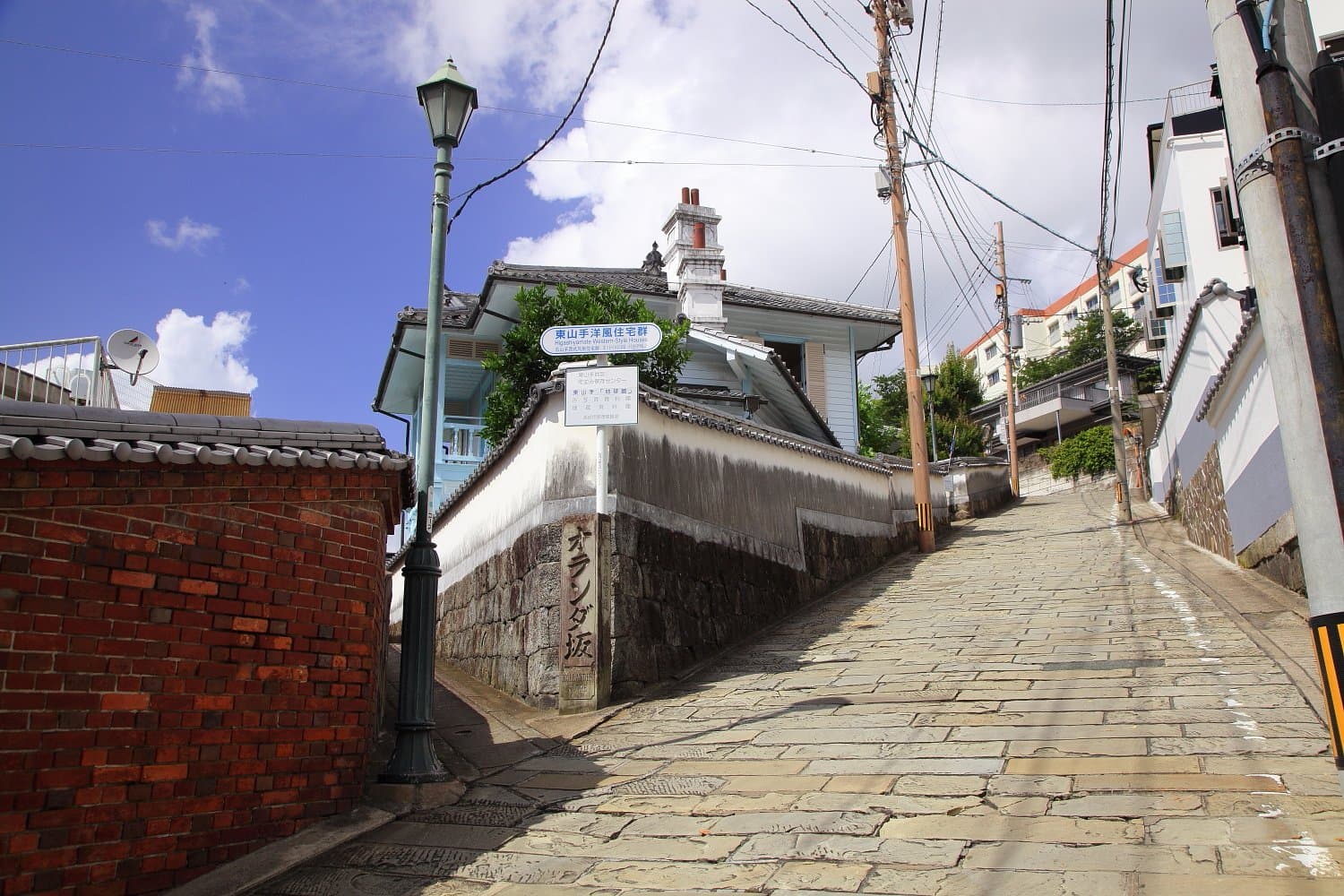 A sloping stone-paved lane between a brick wall, a white plastered wall and a Western-style house