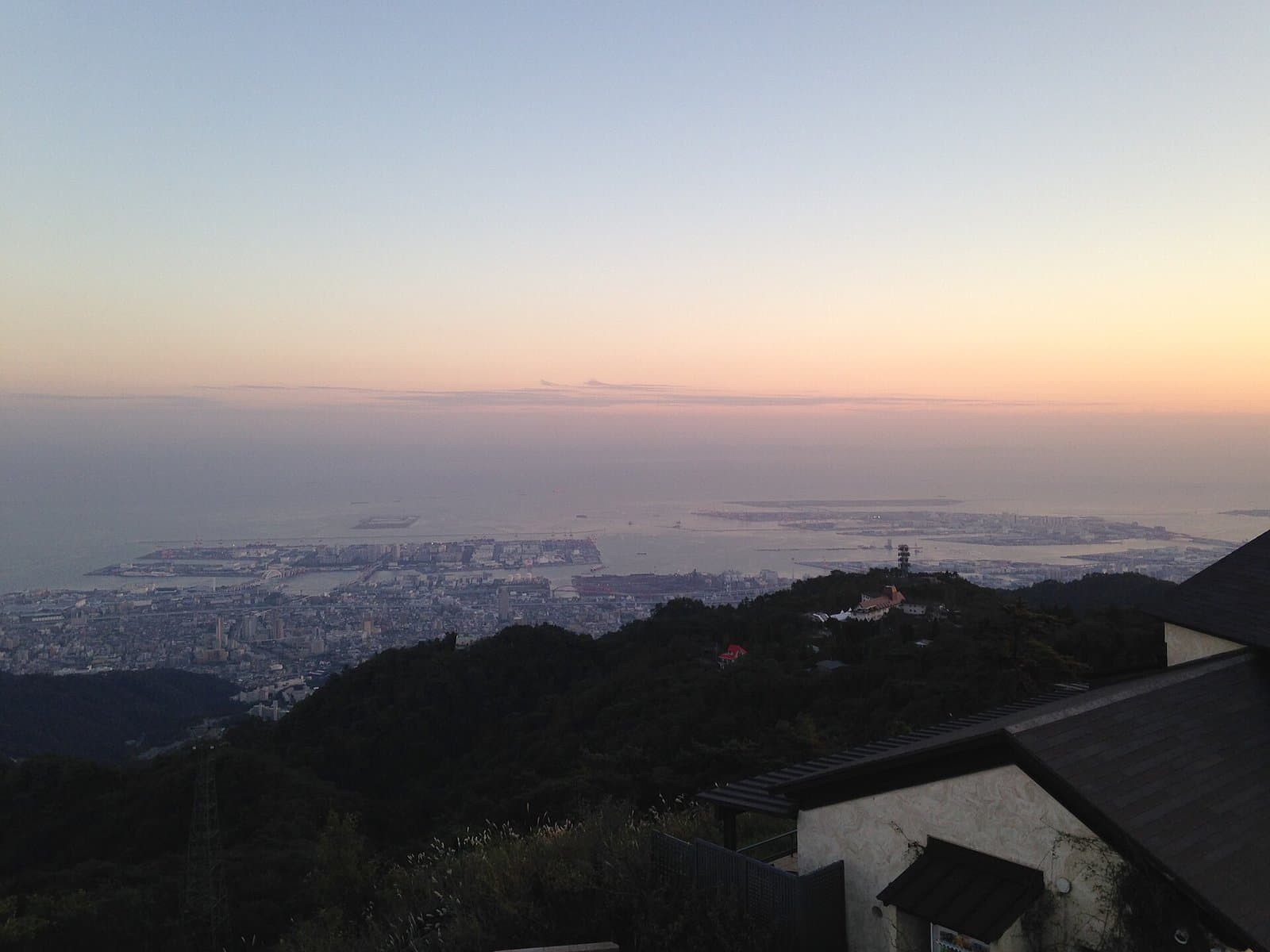 Dusk over Kobe and the sea seen from high on the mountain, with a building roof in the lower right