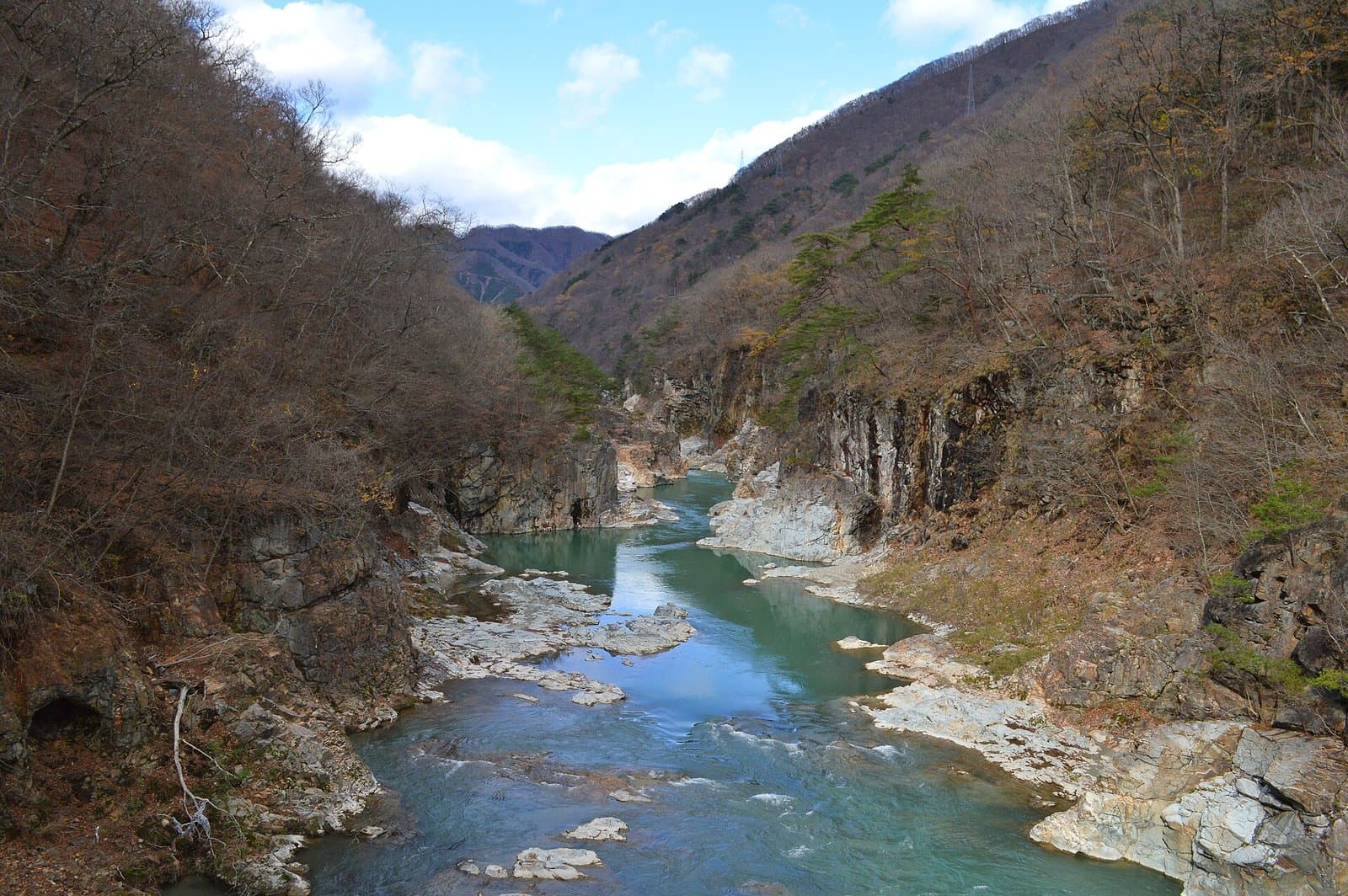 灰色の岩の崖と葉の落ちた山の斜面の間を流れる青緑の川